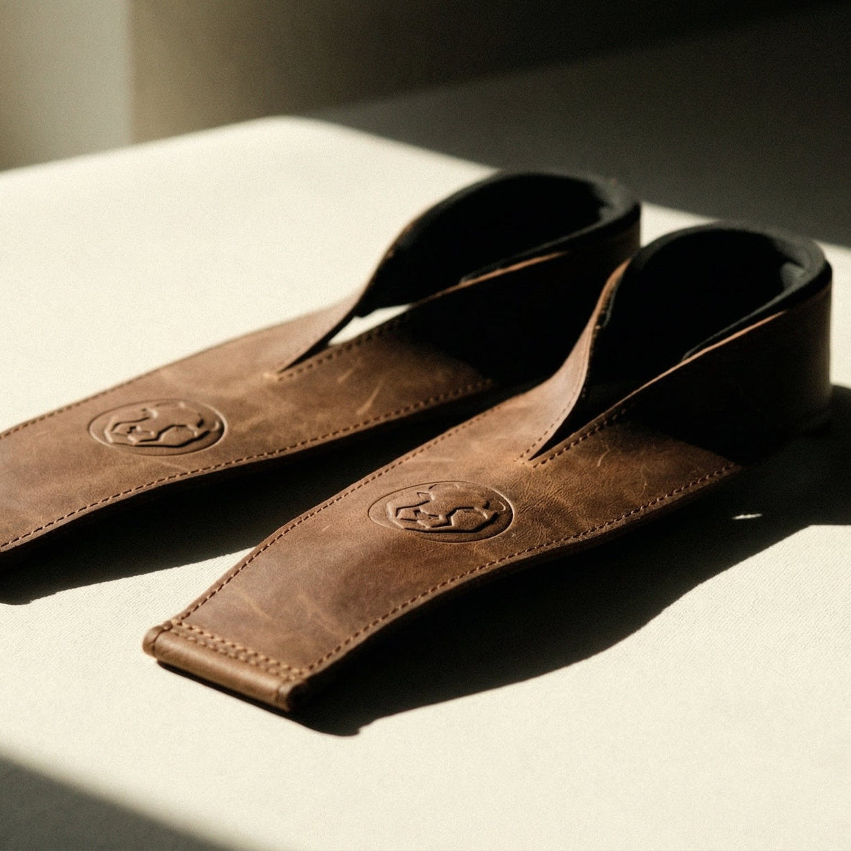 Brown leather Olympic weightlifting straps resting on a light surface in natural window light
